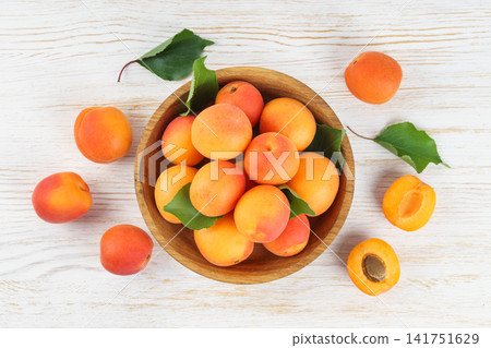 Fresh apricots in wooden bowl with green leaves on white wooden background. Healhy food, ripe friut Fresh apricots in wooden bowl with green leaves on white wooden background. Healhy food, ripe friut 141751629