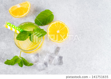 Cold homemade lemonade with fresh lemon, mint and ice in glass on gray background, copy space Cold homemade lemonade with fresh lemon, mint and ice in glass on gray background, copy space 141751635