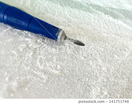 Close-up of a blue electric nail drill with carbide cutter bit covered in white acrylic dust on a table. Ideal for nail salon, manicure service, hardware pedicure, beauty industry, and nail care Close-up of a blue electric nail drill with carbide cutter bit covered in white acrylic dust on a table. Ideal for nail salon, manicure service, hardware pedicure, beauty industry, and nail care 141751748