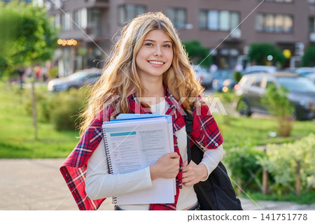 Happy female student with backpack and textbooks standing outside Happy female student with backpack and textbooks standing outside 141751778