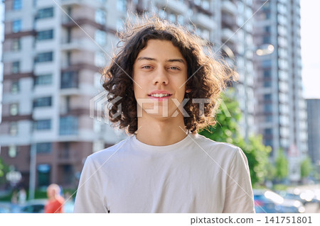 Happy curly haired teenage boy smiling outdoors on modern city street background Happy curly haired teenage boy smiling outdoors on modern city street background 141751801