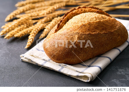 loaf of wheat bread with sourdough with ears of wheat on dark kitchen table, selective focus loaf of wheat bread with sourdough with ears of wheat on dark kitchen table, selective focus 141751876