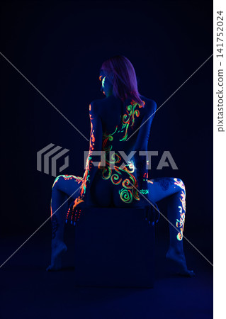 Woman with glowing neon body paint in dark studio Woman with glowing neon body paint in dark studio 141752024