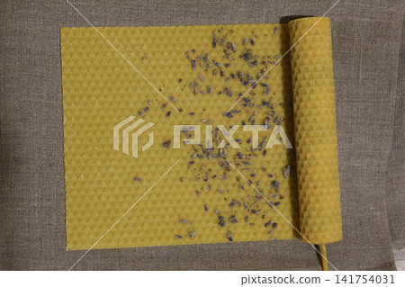 Overhead View of a Partially Rolled Handmade Yellow Beeswax Honeycomb Candle with Scattered Dried Lavender Buds Overhead View of a Partially Rolled Handmade Yellow Beeswax Honeycomb Candle with Scattered Dried Lavender Buds 141754031