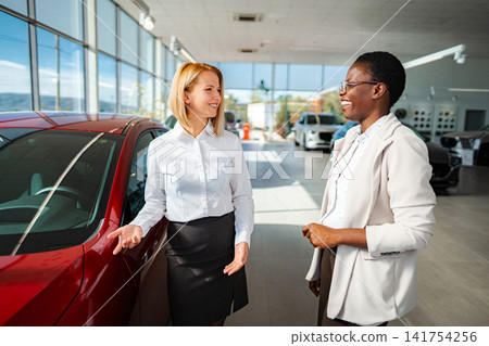 Saleswoman talking with customer about car at dealership showroom Saleswoman talking with customer about car at dealership showroom 141754256