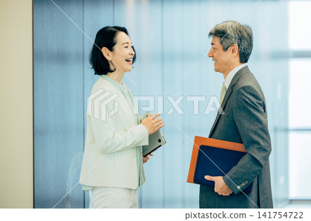 身著西裝的高級男女在辦公室走廊交談。 身著西裝的高級男女在辦公室走廊交談。 141754722