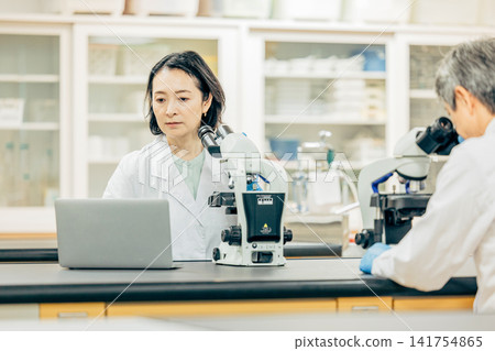 在實驗室中使用顯微鏡進行研究的研究人員 在實驗室中使用顯微鏡進行研究的研究人員 141754865