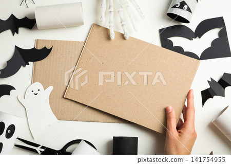Halloween. Hand reaching for blank cardboard amidst colorful halloween crafts Halloween. Hand reaching for blank cardboard amidst colorful halloween crafts 141754955