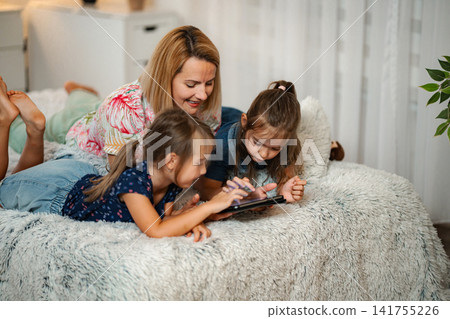 Mother and daughters enjoying tablet content together at home Mother and daughters enjoying tablet content together at home 141755226