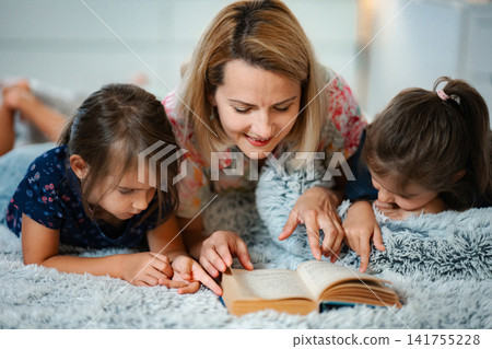 Mother and daughters reading story book together in bed Mother and daughters reading story book together in bed 141755228