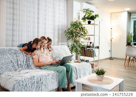 Mother and daughters enjoying laptop together in living room Mother and daughters enjoying laptop together in living room 141755229