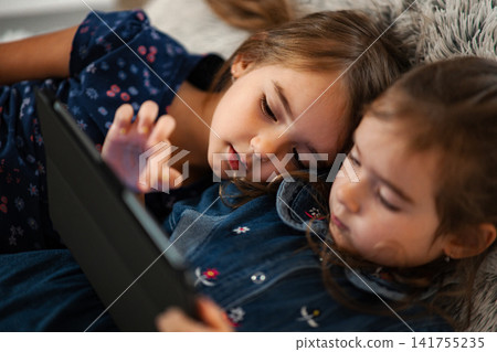 Little girls watching digital tablet together on sofa Little girls watching digital tablet together on sofa 141755235