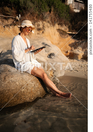 Woman working remotely on a tablet at sunny beach Woman working remotely on a tablet at sunny beach 141755480