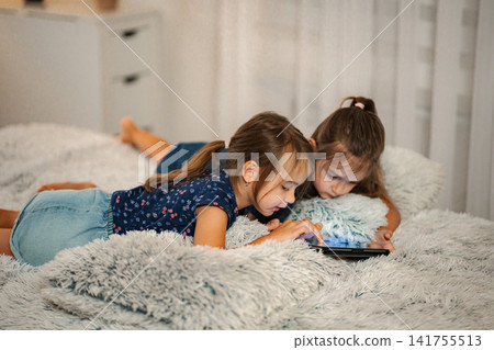 Two young girls using digital tablet on bed at home Two young girls using digital tablet on bed at home 141755513
