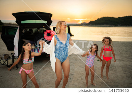 Mother and three young girls dancing on beach at sunset 141755660