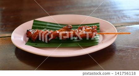 Grilled meat skewer plate banana leaf on wooden table with savory glaze Grilled meat skewer plate banana leaf on wooden table with savory glaze 141756118