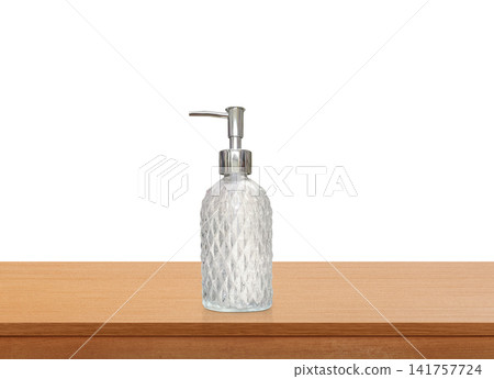A clear glass perfume bottle with a diamond pattern on a wooden table. A clear glass perfume bottle with a diamond pattern on a wooden table. 141757724