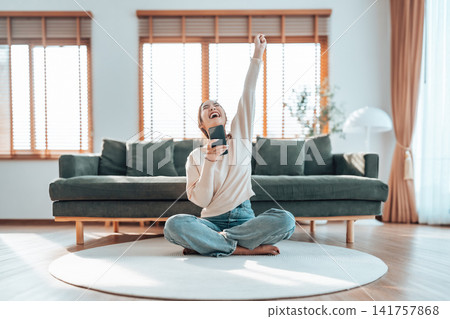 Smiling pretty young Asian woman sitting on cozy couch Smiling pretty young Asian woman sitting on cozy couch 141757868