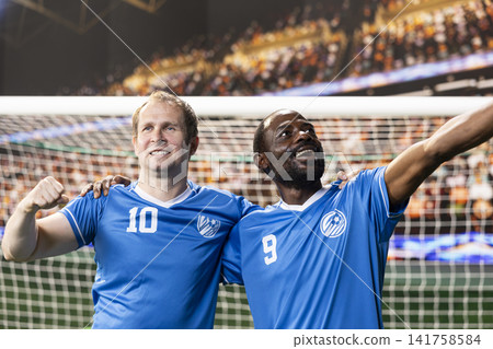 Football players in blue uniforms enjoying passionate goal celebration, cheering together on pitch and hugging. Joy after winning competitive stadium match, arms raised. Football players in blue uniforms enjoying passionate goal celebration, cheering together on pitch and hugging. Joy after winning competitive stadium match, arms raised. 141758584