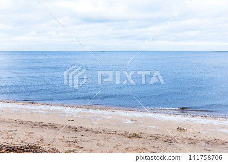 A calm, empty sandy beach meets a blue sea at the distant horizon 141758706