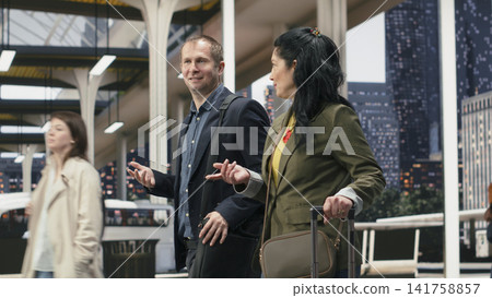 Business travelers walk together through bus terminal while discussing their work journey. Business companions share conversation on coach station departure platform Business travelers walk together through bus terminal while discussing their work journey. Business companions share conversation on coach station departure platform 141758857
