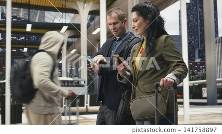 Relaxed coworkers in bus station check route details together with smartphone and boarding pass. Businesspeople doing online bus ticket checkin with mobile phone app Relaxed coworkers in bus station check route details together with smartphone and boarding pass. Businesspeople doing online bus ticket checkin with mobile phone app 141758897