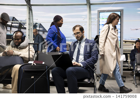 CEO man in airport terminal lounge working on laptop during international business trip. Businessman wearing formal attire waiting for plane arrival, finishing tasks on notebook device CEO man in airport terminal lounge working on laptop during international business trip. Businessman wearing formal attire waiting for plane arrival, finishing tasks on notebook device 141759008
