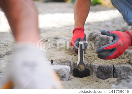 Workers lay stones for a pathway in a garden area Workers lay stones for a pathway in a garden area 141759046