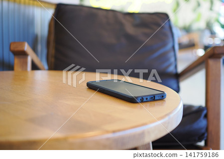 Black smartphone on wooden table in cafe setting. lost smart phone concept Black smartphone on wooden table in cafe setting. lost smart phone concept 141759186