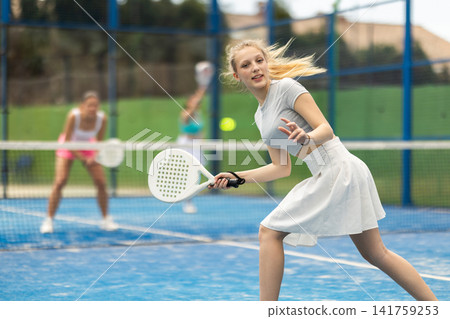Young woman playing paddle tennis against team of women Young woman playing paddle tennis against team of women 141759253