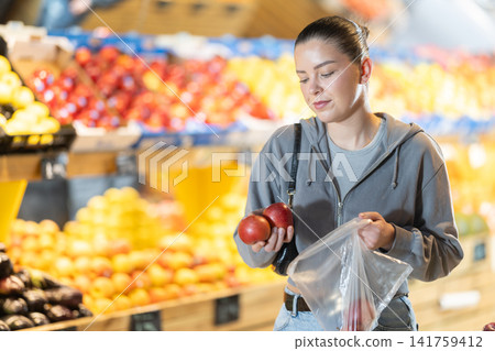 Woman choosing ripe apples in supermarket, she holding a weighing bag Woman choosing ripe apples in supermarket, she holding a weighing bag 141759412