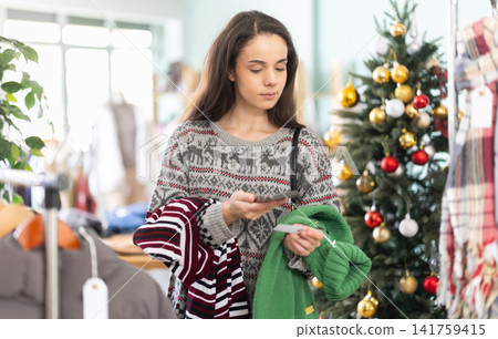 Young girls scanning QR-code on sweaters in clothing store during Christmas Young girls scanning QR-code on sweaters in clothing store during Christmas 141759415