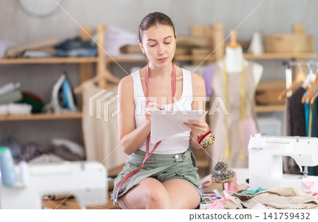 female dressmaker deals with documents in the atelier female dressmaker deals with documents in the atelier 141759432