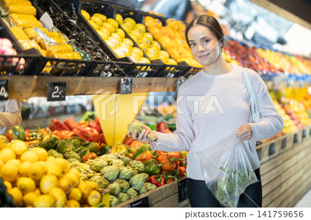woman stands in a supermarket near the shelves and chooses artichokes woman stands in a supermarket near the shelves and chooses artichokes 141759656