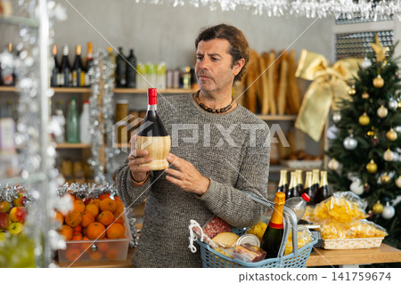 Thoughtful shopper selecting alcoholic drinks for Christmas festivities in grocery store Thoughtful shopper selecting alcoholic drinks for Christmas festivities in grocery store 141759674