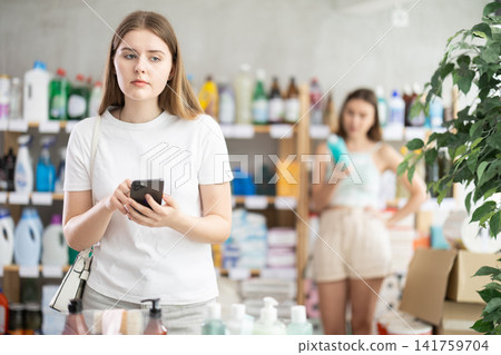 Girl holding phone and looking around in supermarket Girl holding phone and looking around in supermarket 141759704