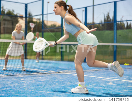 Young woman playing paddle tennis against team of women Young woman playing paddle tennis against team of women 141759755