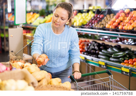 Middle-aged woman purchaser buying onions in grocery store Middle-aged woman purchaser buying onions in grocery store 141759788