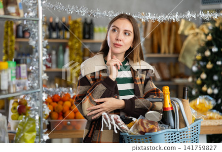 Portrait of female customer with cart choosing food and wine for Christmas celebration in grocery department of supermarket Portrait of female customer with cart choosing food and wine for Christmas celebration in grocery department of supermarket 141759827