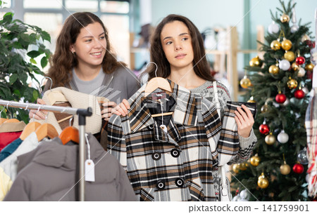 Young girls choosing coat or jacket in clothing store during Christmas Young girls choosing coat or jacket in clothing store during Christmas 141759901