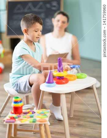 Child psychologist asks boy to play game: using both hands to simultaneously navigate maze drawn on board 141759960