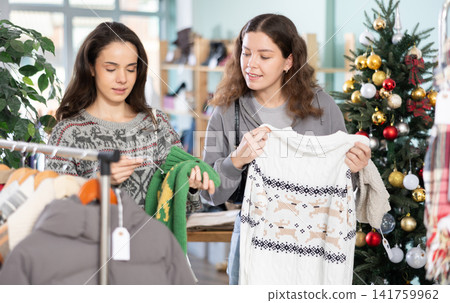 Two women choose knitted sweaters against the background of a Christmas tree Two women choose knitted sweaters against the background of a Christmas tree 141759962