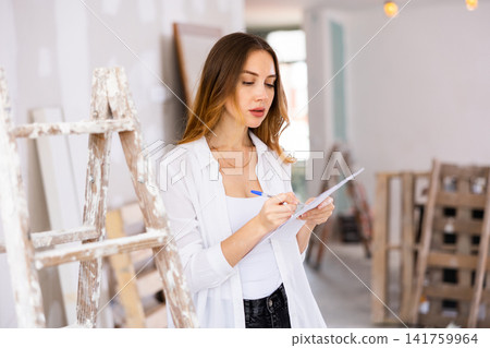 Woman designer checking documents during repair works Woman designer checking documents during repair works 141759964