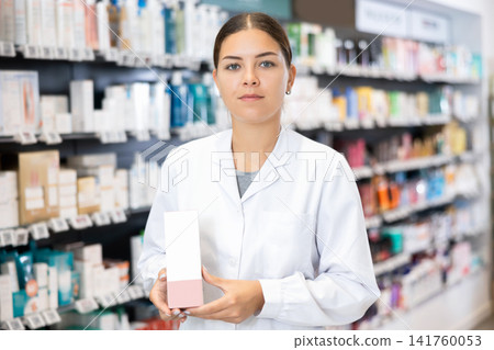 In pharmacy, female specialist holds and shows new effective remedy for moisturizing delicate skin 141760053