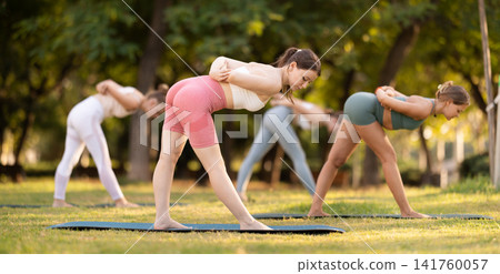 Athletic girls meditates in yoga pose parshvottanasana in summer sunny park. Demonstration of various yoga poses Athletic girls meditates in yoga pose parshvottanasana in summer sunny park. Demonstration of various yoga poses 141760057