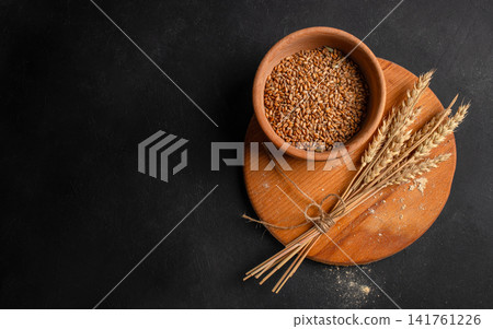 Wheat grains and wheat ears on wooden board over dark background with copy space Wheat grains and wheat ears on wooden board over dark background with copy space 141761226