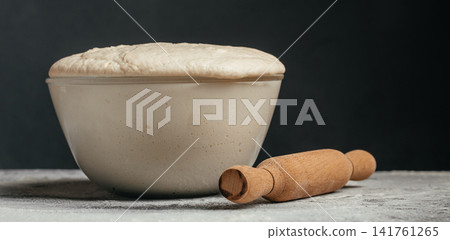 Proofed bread dough rising in glass bowl with rolling pin Proofed bread dough rising in glass bowl with rolling pin 141761265