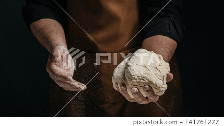 Baker holding fresh bread dough with floating flour particles Baker holding fresh bread dough with floating flour particles 141761277