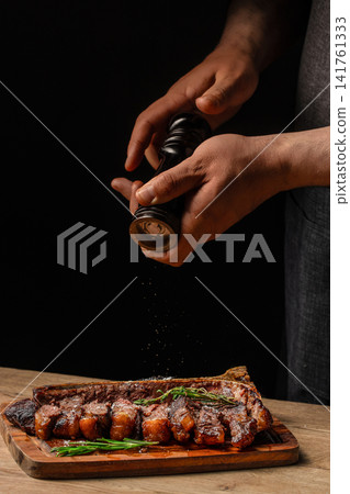 Chef seasoning sliced porterhouse steak with pepper on wooden serving board 141761333