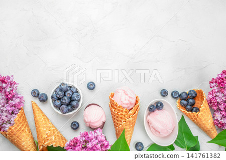 Strawberry ice cream in waffle cones with blueberries and lilac flowers, summer dessert background Strawberry ice cream in waffle cones with blueberries and lilac flowers, summer dessert background 141761382